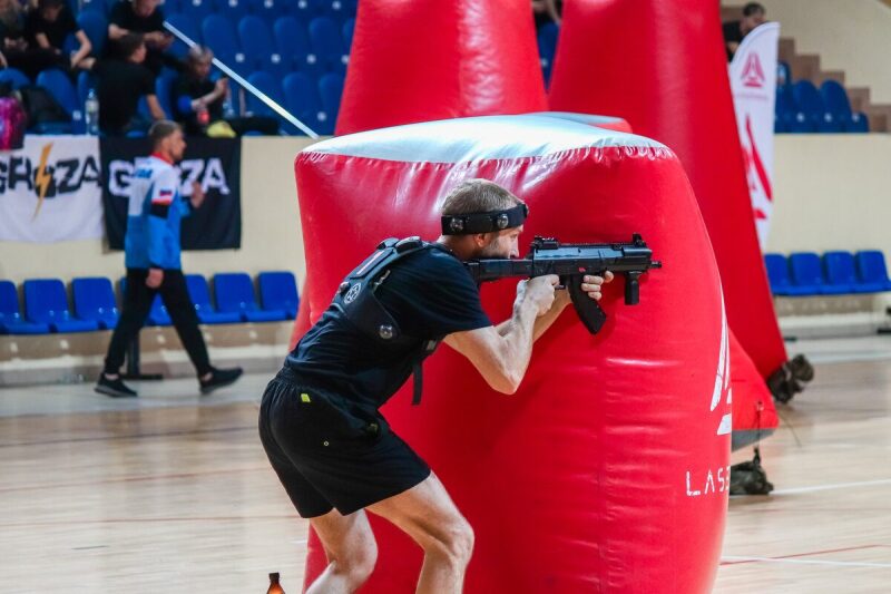 Боец LASERWAR прицеливается из-за массивного красного укрытия.